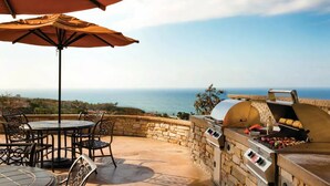 Une terrasse extérieure avec un mur en pierre, un barbecue et une table avec des chaises.