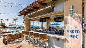 Un espace bar extérieur avec vue sur la piscine, des tabourets de bar et un panneau indiquant le point de commande.
