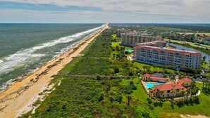 Un complejo turístico frente al mar con propiedades en la playa, piscina y un gran edificio de hotel.