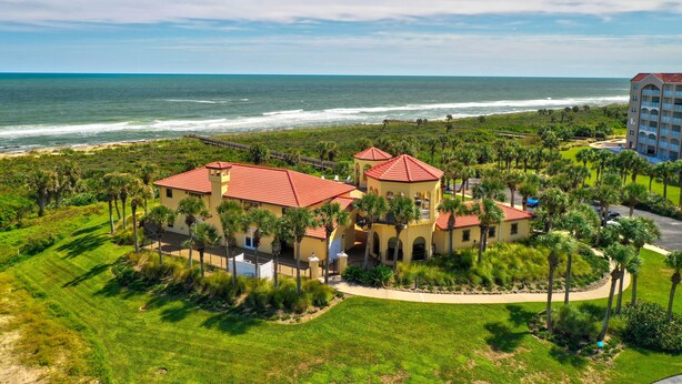 Un hotel costero con varias edificaciones, vista a la playa y un césped bien cuidado con palmeras.