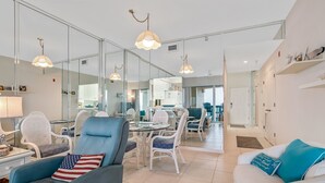 Una sala de estar moderna con un sillón azul, un sofá blanco y una zona de comedor con sillas blancas y una mesa de vidrio.