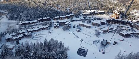Un centro de esquí cubierto de nieve con varias construcciones tipo chalet, telesillas y una pista de esquí.