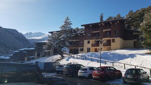 Hotel amb diverses plantes, zona d'aparcament amb cotxes i una muntanya nevada al fons.