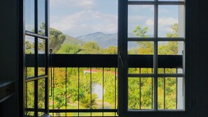 A room with a large window offering a view of a mountainous landscape and greenery. - Wonderful place 3* with view and pool (Montesquieu-des-Albères)