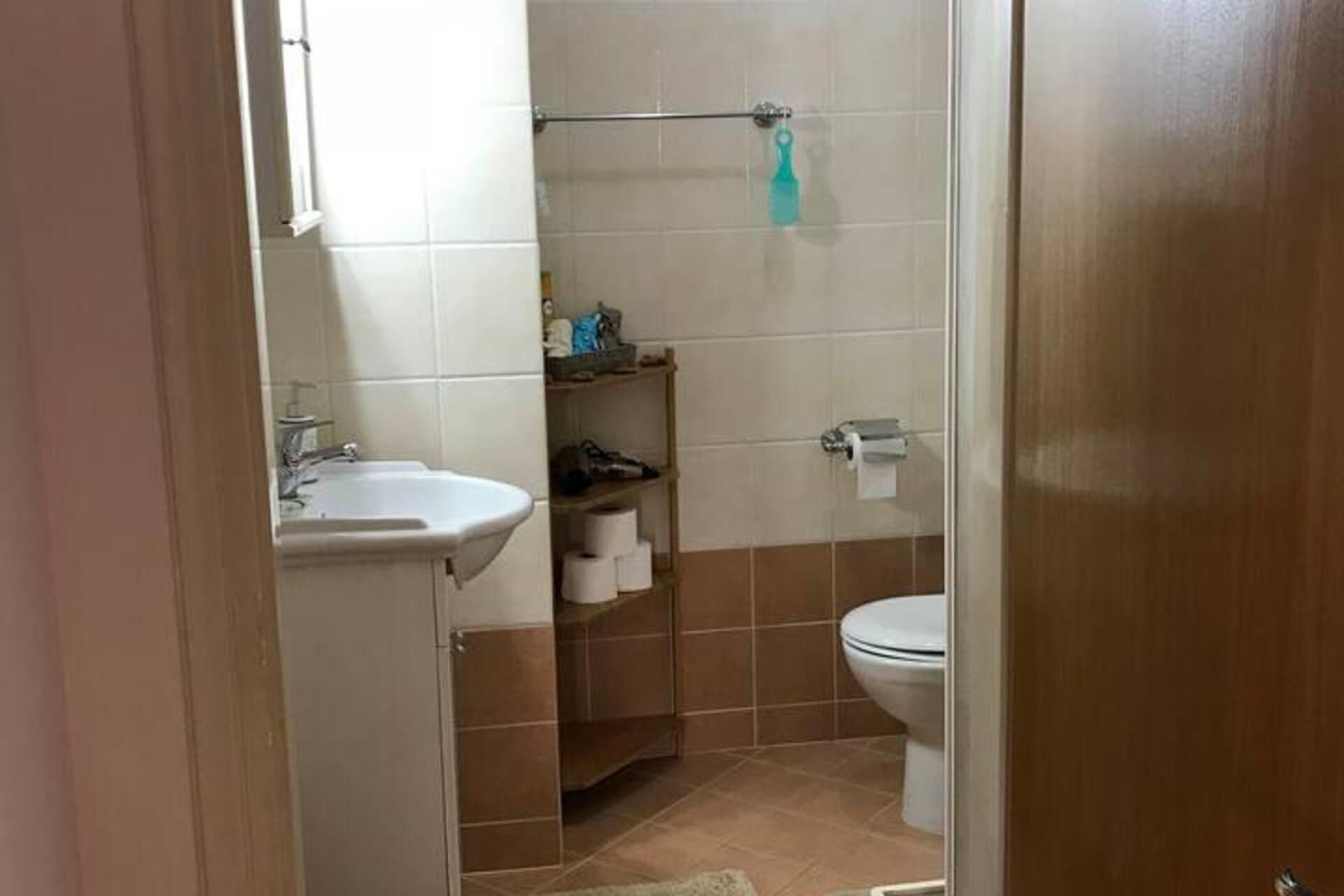 A bathroom with a sink, toilet, and shelves with toiletries.