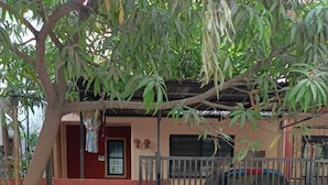 A gated residential area with a parked car, a tree, and a building with a red door and window.