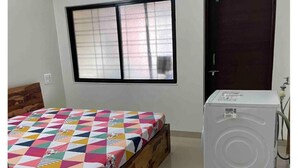 A bedroom with a wooden bed, a colorful quilt, an air conditioner, a window with blinds, and a door.