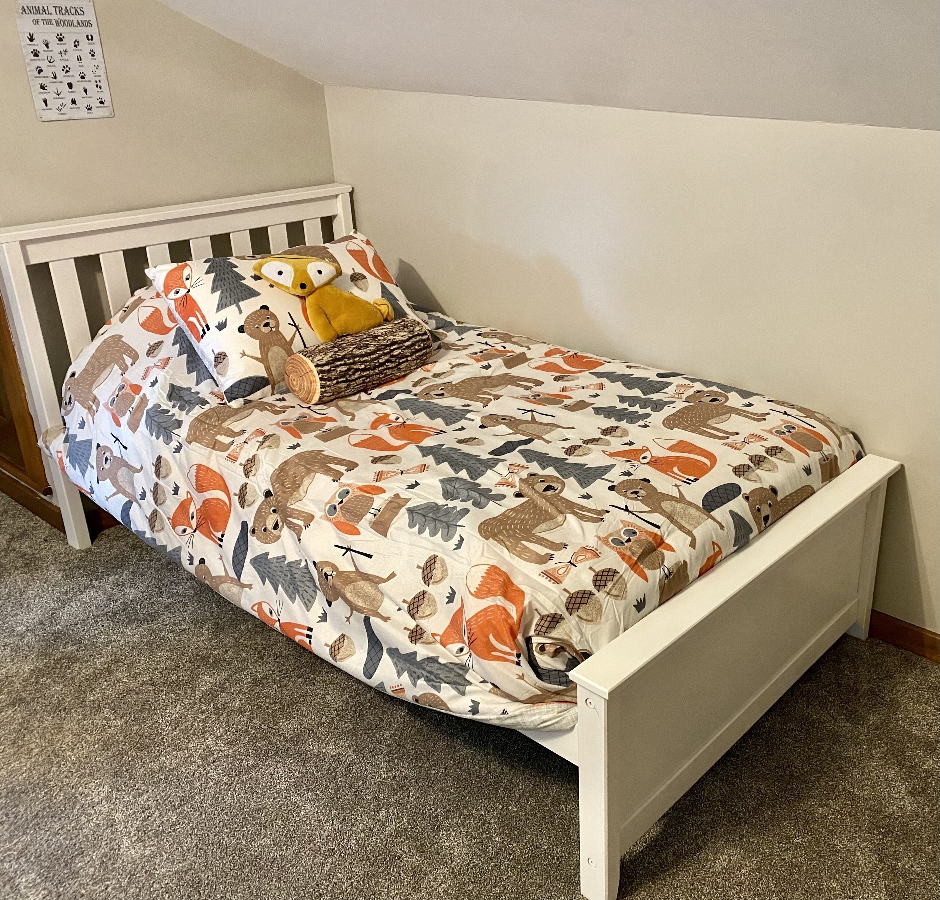 A single bed with a white frame, a patterned bedspread, and a pillow with animal prints.