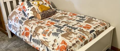 A single bed with a white frame, a patterned bedspread, and a pillow with animal prints.