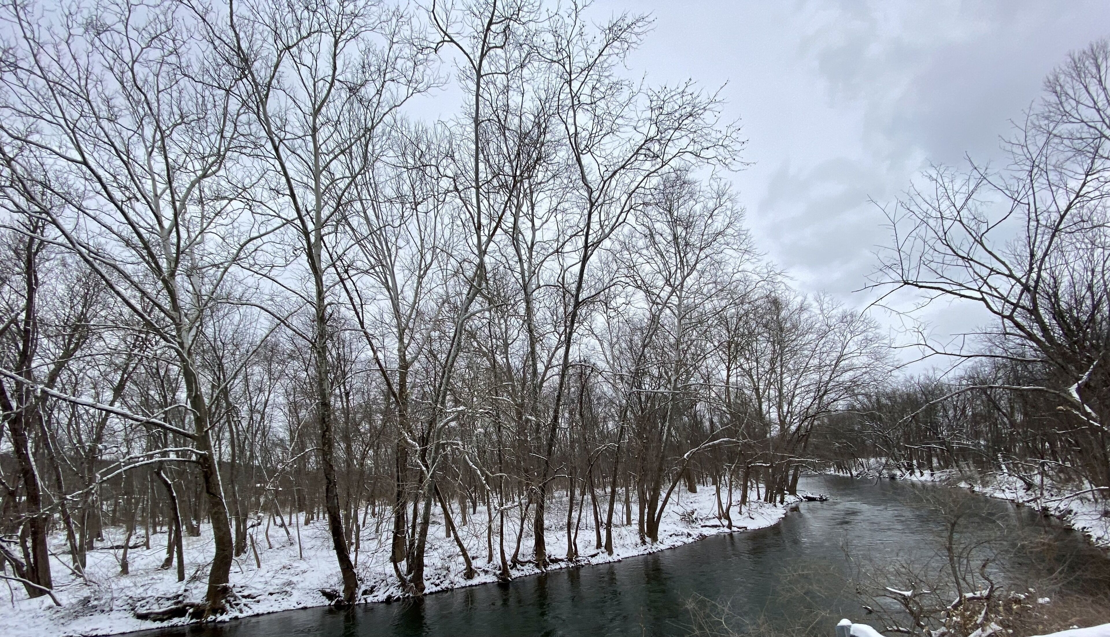 A snow-covered river with bare trees on both sides.