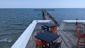 A pier extending into the sea with tables and chairs for dining. - Club Paradise Beach Condo-Top Floor, Ocean View, King Bed, Pet Friendly (Galveston)