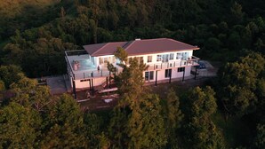 Una casa moderna de dos pisos con una amplia terraza y piscina, rodeada de un bosque frondoso.