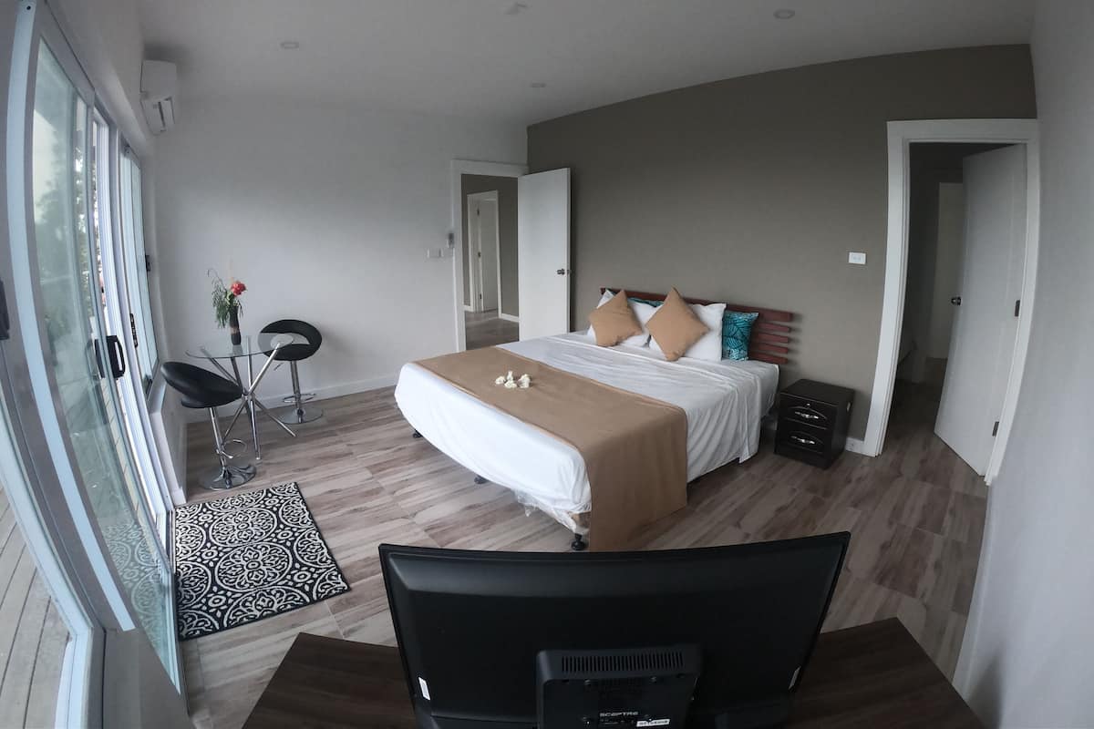 A modern bedroom with a large bed, a desk, and a chair. There is a window and a door visible.
