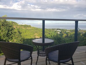 A balcony with wicker chairs and a small round table, overlooking a lush landscape with a view of the ocean and distant hills. - Belle Balise (Korolevu)
