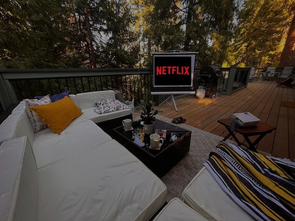 Een terras buiten met een witte bank, een salontafel en een Netflix-bord.