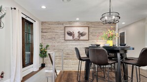 A dining area with a wooden wall, a framed artwork, a chandelier, and a table with chairs.