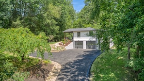 A two-story house with a garage, surrounded by lush greenery and trees.