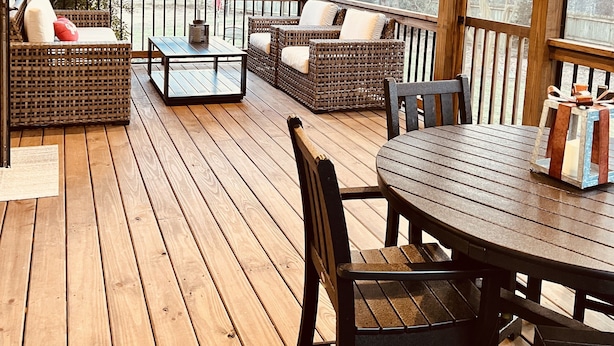 A covered outdoor deck with wooden flooring, wicker furniture, and a table with chairs.