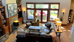 A cozy living room with a fireplace, comfortable seating, and large windows offering a view of the outdoors.