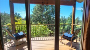 A balcony with two rocking chairs, a wooden deck, and a view of trees and hills.