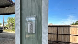 Un poste de madera con una cubierta de plástico transparente, un objeto metálico y un área de césped con una valla de madera al fondo.