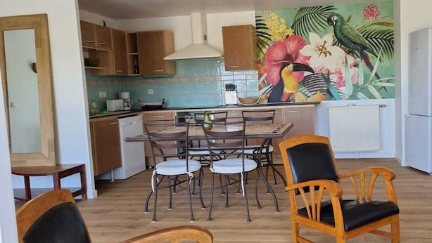 A compact kitchen with a dining area, a refrigerator, and a mural with tropical birds and flowers. - Grand F3, Avec Balcon Plein sud Sans vis à vis (Vannes)