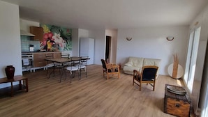 A spacious living area with a wooden floor, a dining table with chairs, a sofa, and a kitchen in the background. - Grand F3, Avec Balcon Plein sud Sans vis à vis (Vannes)
