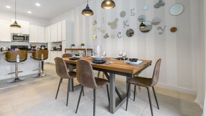 A modern kitchen with white cabinets, a wooden dining table, and bar stools. - Wonderful 4 Bd private pool near Disney Parks (Davenport)