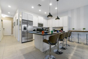 A modern kitchen with white cabinets, stainless steel appliances, and a central island with bar stools.