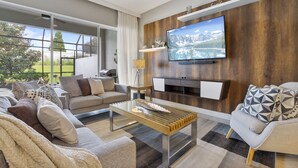 A modern living room with a large TV, comfortable sofas, and a wooden accent wall. - Wonderful 4 Bd private pool near Disney Parks (Davenport)
