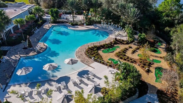 A pool area with lounge chairs and umbrellas, surrounded by greenery and a golf course. - Wonderful 4 Bd private pool near Disney Parks (Davenport)