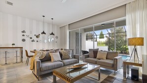 A modern living room with two sofas, a glass coffee table, and a dining area with a bar stool. - Wonderful 4 Bd private pool near Disney Parks (Davenport)