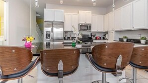 A modern kitchen with white cabinets, stainless steel appliances, and wooden bar stools. - Wonderful 4 Bd private pool near Disney Parks (Davenport)