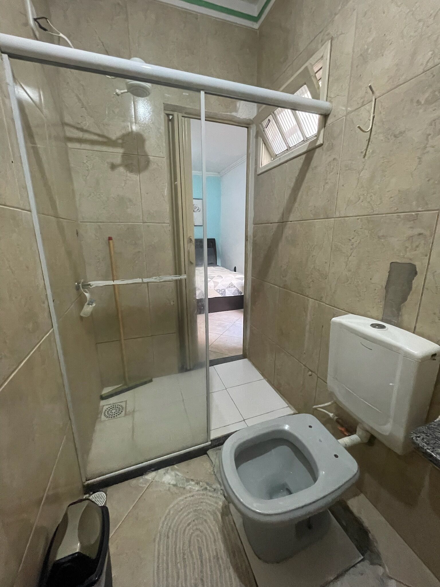 A small bathroom with a shower, toilet, and a visible door leading to another room.