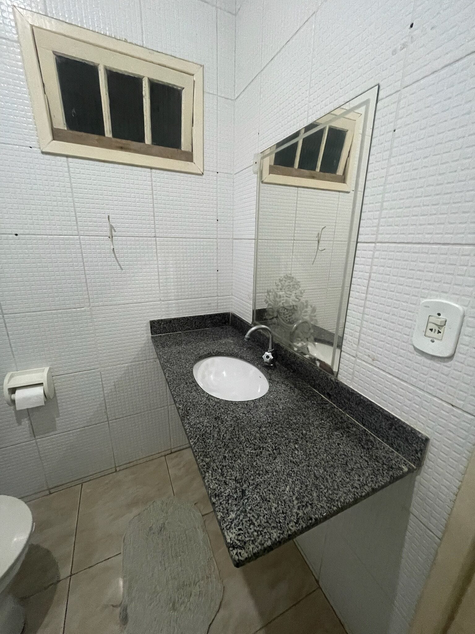 Een badkamer met een witte wastafel, een spiegel, een raam en een toilet.