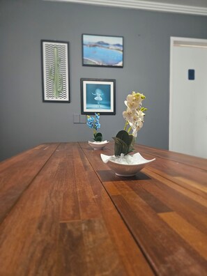 A wooden table with three white ceramic bowls containing white flowers, set against a grey wall with framed pictures. - Hope Hostel (Guarapari)
