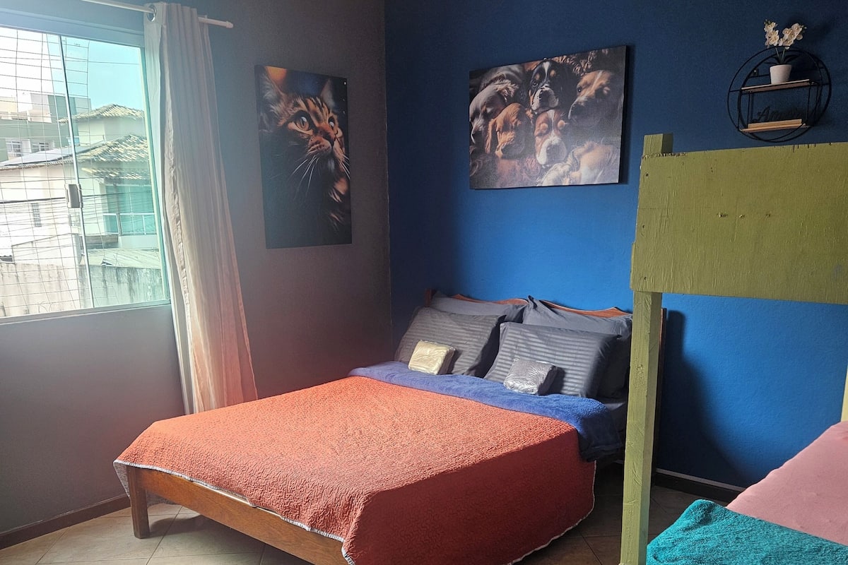 A bedroom with a bed, a bunk bed, a window with curtains, and two wall art pieces.