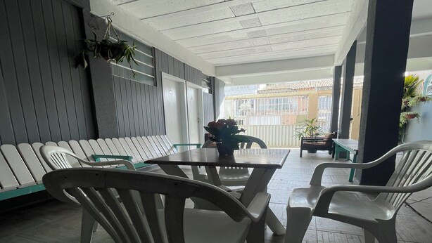 A covered outdoor seating area with plastic chairs and a table, surrounded by walls and a patterned ceiling. - Hope Hostel (Guarapari)