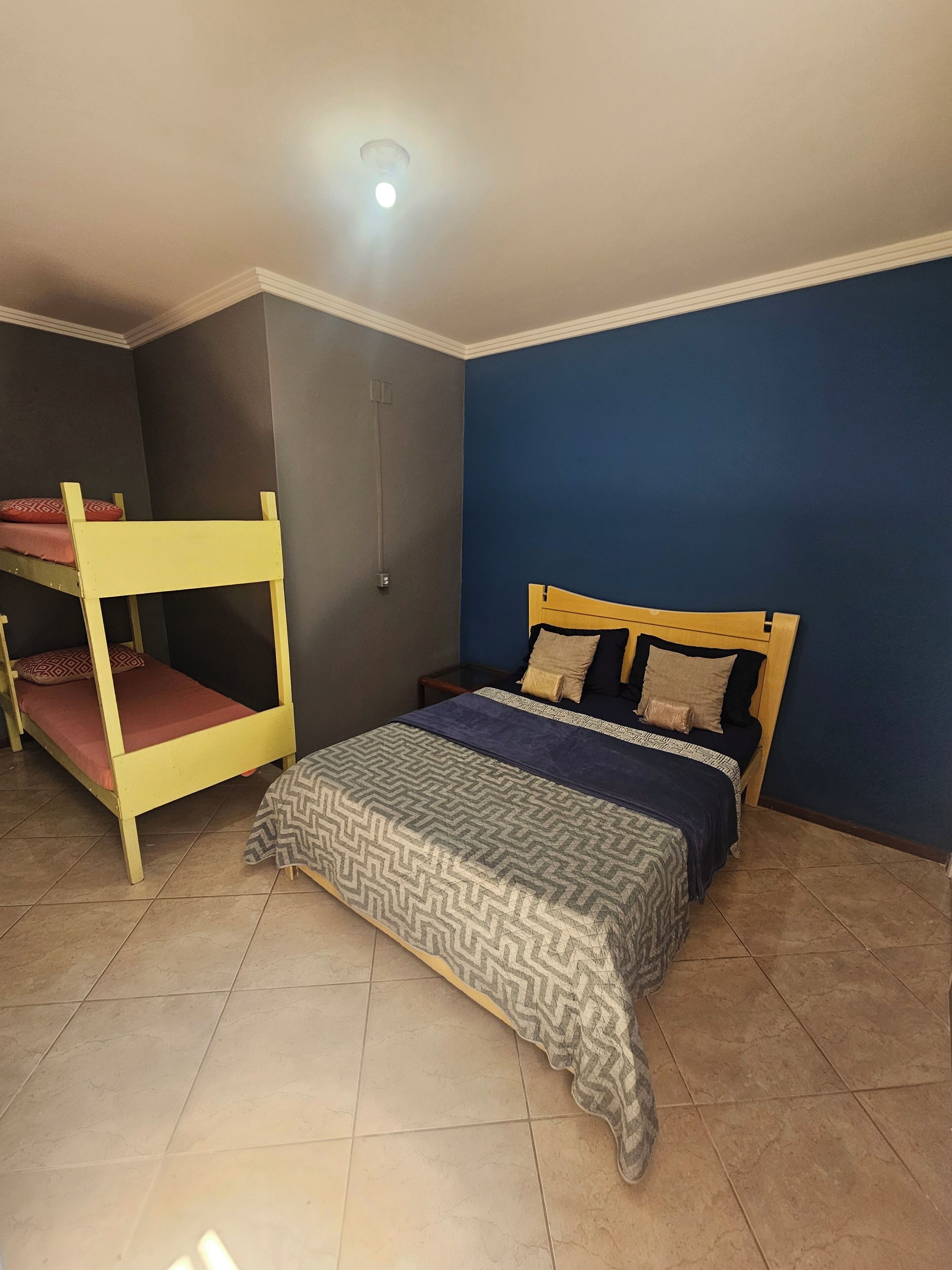 A room with a bunk bed, a single bed, and a tiled floor.