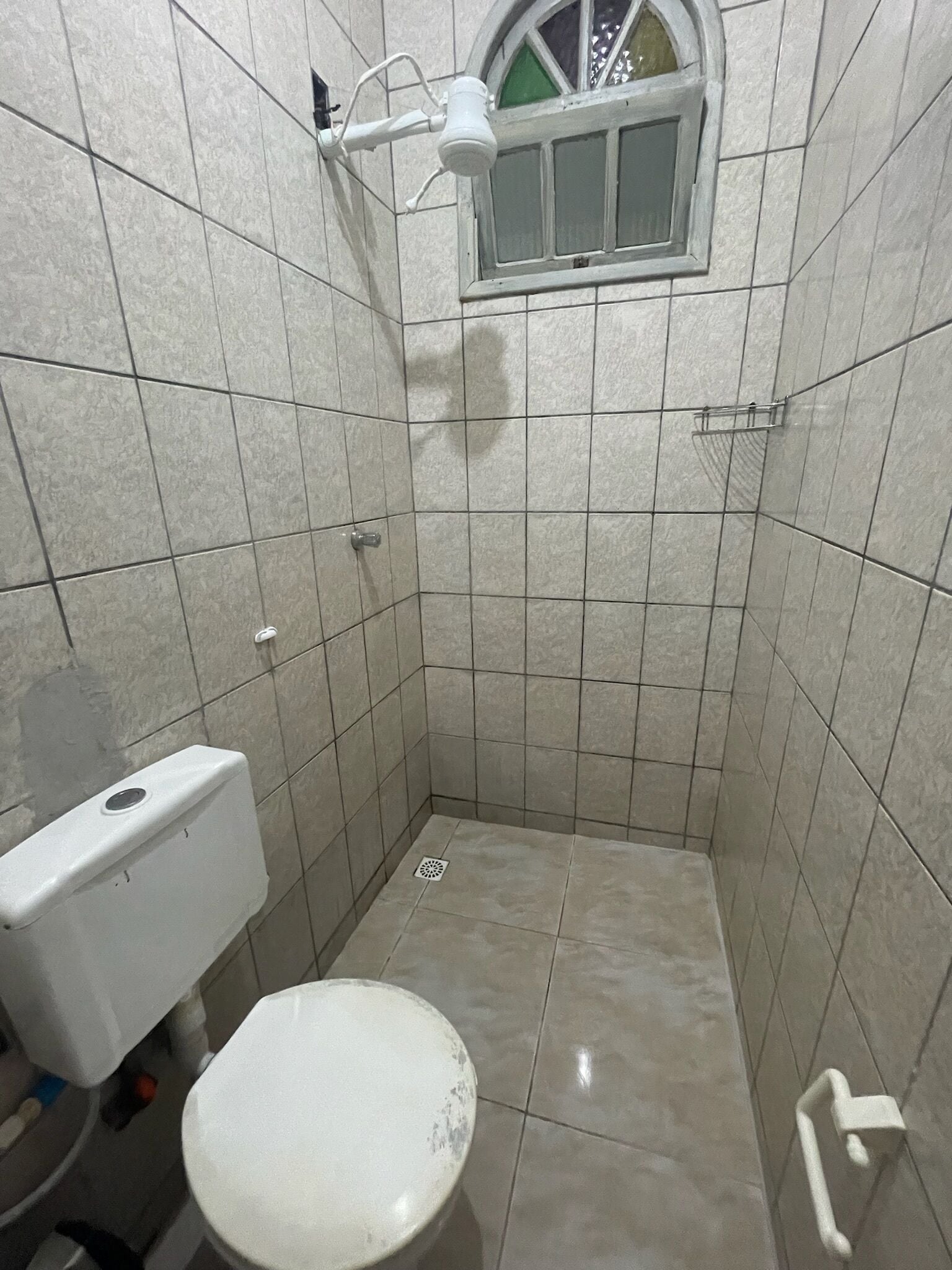 A small, tiled bathroom with a toilet, a window, and a shower area.