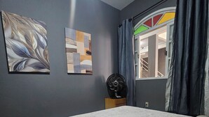 A bedroom with a bed, a standing fan, and abstract wall art. - Hope Hostel (Guarapari)