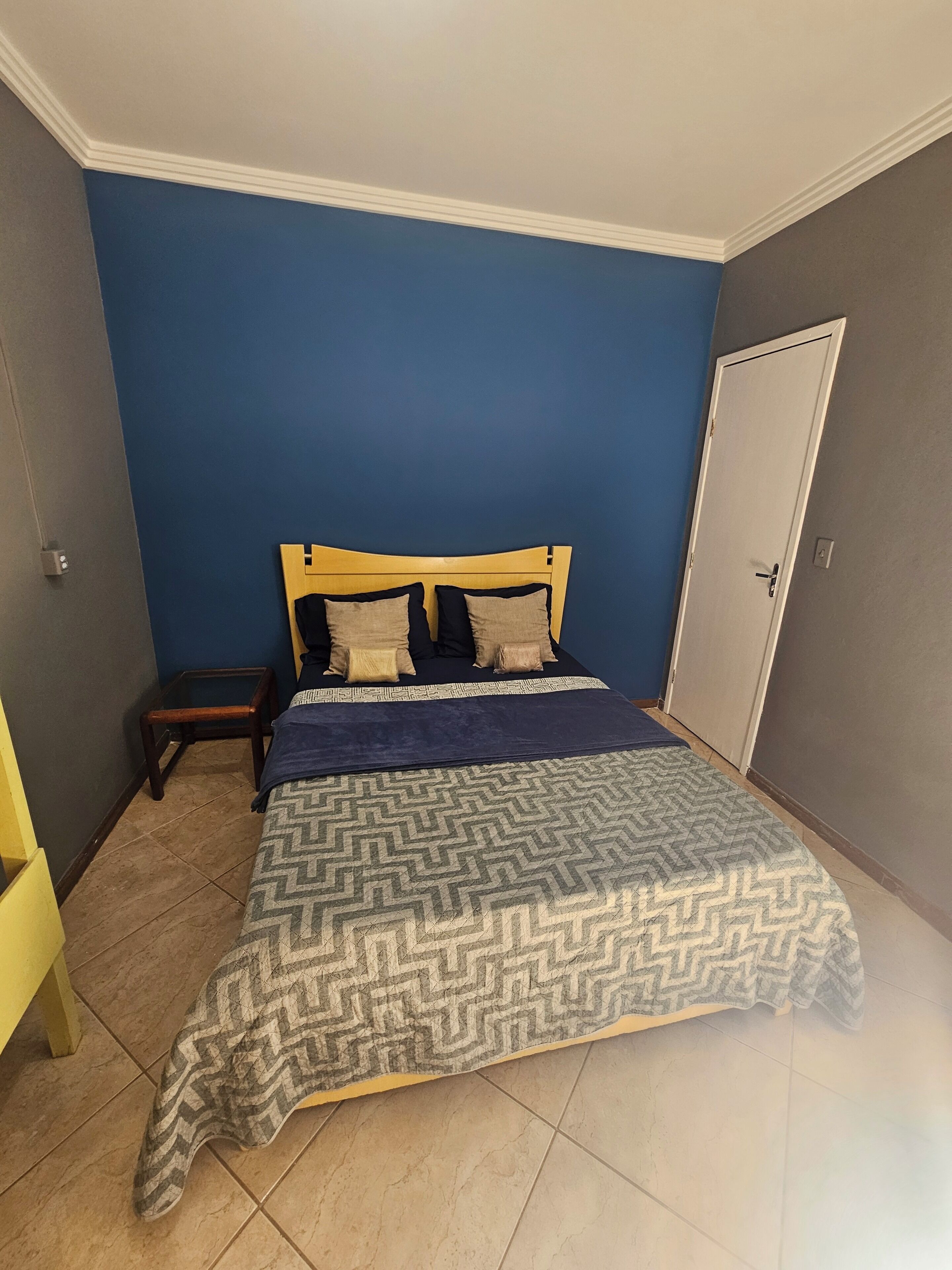 A bedroom with a bed, a nightstand, a door, and a wall with a blue color.
