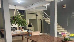 A spacious dining area with a granite table, chairs, and a hanging plant. A staircase leads to an upper level. - Hope Hostel (Guarapari)
