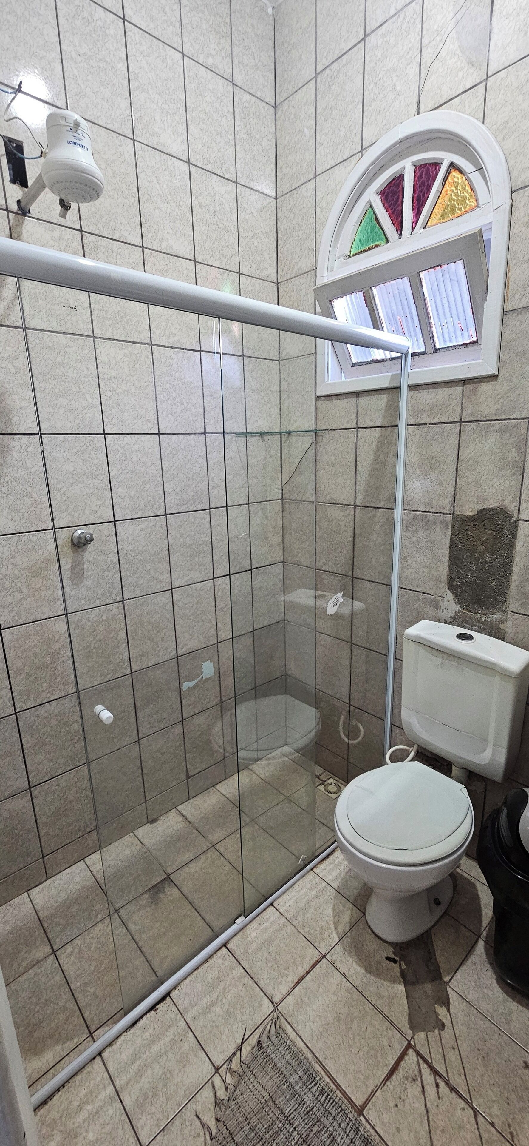 Une salle de bain dotée d’une douche à parois de verre, de toilettes et d’une fenêtre ornée de vitraux.