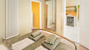 Habitación de hotel con cama, toallas, radiador, espejo y vista al área de lavandería.