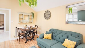 Una sala de estar con un sofá verde, almohadas amarillas, una mesa de comedor de madera y un reloj de pared.