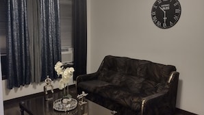 Una sala de estar con un sofá de cuero marrón oscuro, una mesa de centro con objetos decorativos, un reloj de pared y una lámpara de techo.