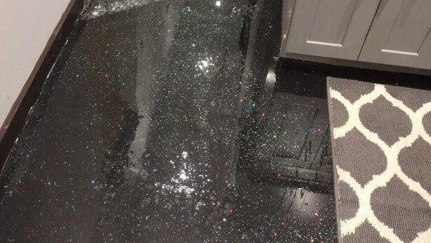 Un estrecho pasillo con piso brillante y reflectante, un tapete estampado y muebles de cocina modernos.