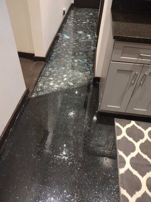 A narrow hallway with a shiny, reflective floor, a patterned rug, and modern cabinetry.