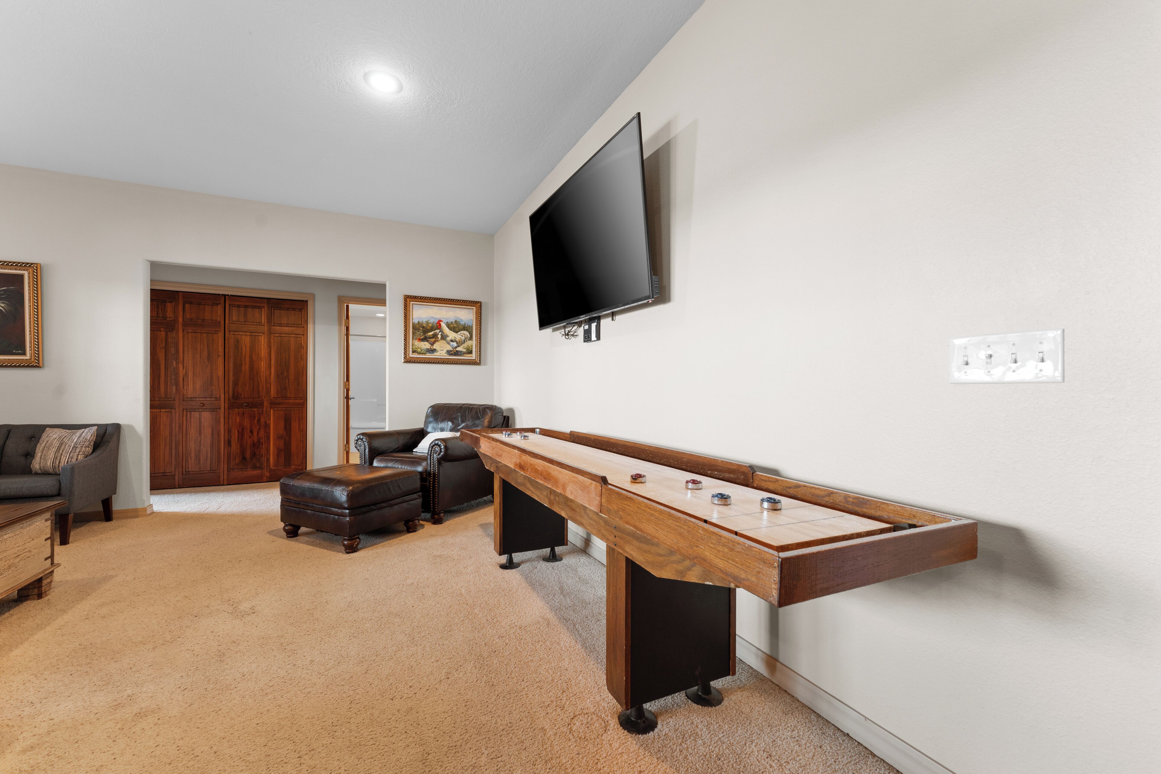 A room with a pool table, a television mounted on the wall, a couch, and a door leading to another room.
